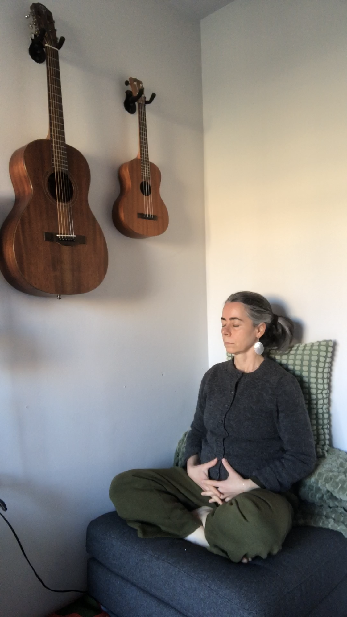 Julia meditating with her music instruments on the wall.